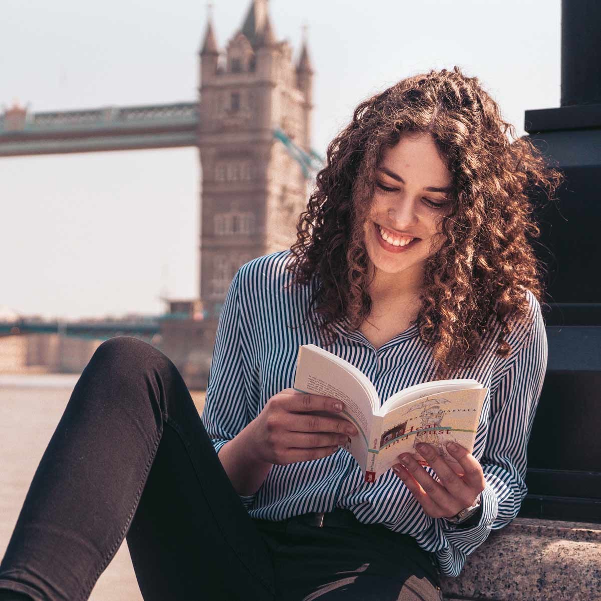 Eine Auslandsstudentin liest ein Buch vor der Tower Bridge in England